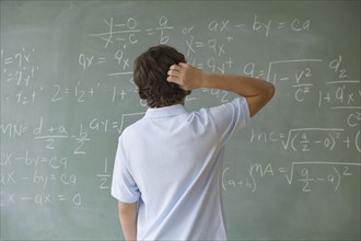 Teenaged boy looking at math equations on blackboard.