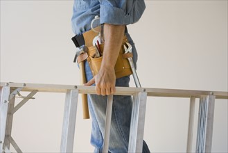 Man wearing tool belt and holding ladder.