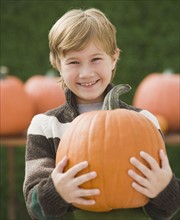 Boy holding pumpkin outdoors.