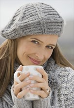 Woman in hat and sweater holding coffee mug.