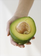 Woman holding halved avocado.
