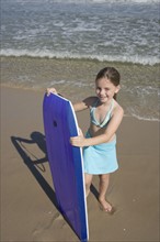 Girl holding boogie board at beach.