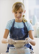 Teenaged girl sculpting on pottery wheel.