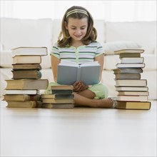 Girl reading next to stacks of books.