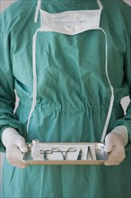 Doctor holding tray of medical instruments.