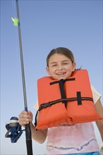 Girl in life jacket holding fishing pole.