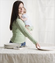 Mother holding baby and setting the table. Date : 2006
