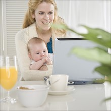 Mother holding baby and using laptop. Date : 2006