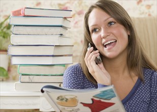 Young woman using cell phone next to stack of books. Date : 2006