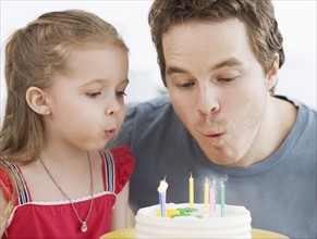 Father and daughter blowing out birthday candles. Date : 2007