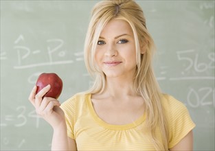 Woman holding apple in front of blackboard. Date : 2007