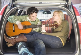 Couple sitting in back of car with guitar. Date : 2007