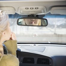 Woman applying lipstick in car rear view mirror. Date : 2007