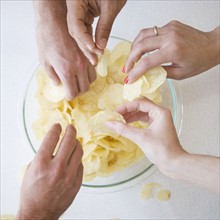 Hands reaching into bowl of chips. Date : 2007