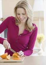 Woman cutting orange in kitchen. Date : 2007