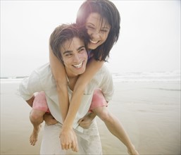 Man giving woman piggyback ride at beach. Date : 2006