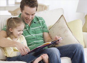Father reading to daughter on sofa. Date : 2007