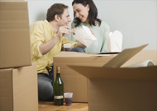 Couple eating take out on boxes in new house. Date : 2006