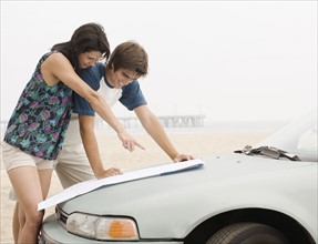 Couple looking at map on car hood at beach. Date : 2006