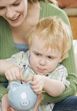 Mother and young son putting change in piggy bank. Date : 2006