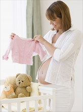 Pregnant woman holding up baby clothing. Date : 2007