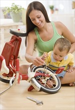 Mother holding baby and fixing tricycle. Date : 2007
