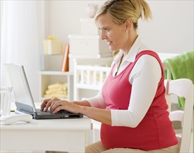 Pregnant woman typing on laptop. Date : 2007