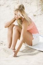 Woman sitting on surfboard at beach. Date : 2007