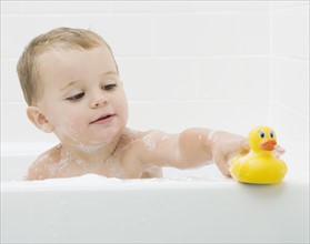 Baby playing with rubber duck in bath. Date : 2007