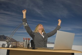 Businesswoman cheering at desk, Salt Flats, Utah, United States. Date : 2007