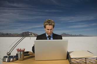 Businessman on salt flats looking at laptop, Salt Flats, Utah, United States. Date : 2007