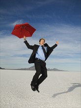 Businessman holding umbrella and jumping, Salt Flats, Utah, United States. Date : 2007