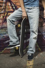 Asian man holding skateboard in front of graffitied wall. Date : 2007