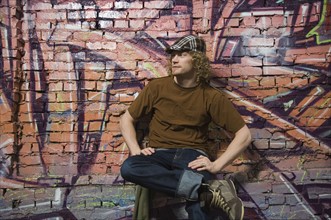 Young man sitting in front of graffitied wall. Date : 2007