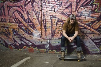Young man with skateboard in front of graffitied wall. Date : 2007