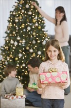 Girl holding Christmas gift in front of family.