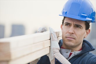 Male construction worker holding stack of lumber.