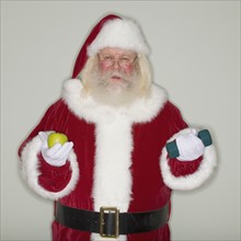 Santa Claus holding apple and dumbbell.