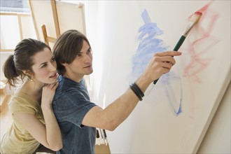 Woman watching boyfriend paint on easel.