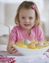 Young girl holding bowl of Easter eggs.