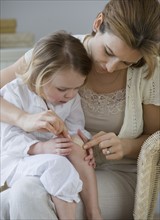 Mother putting bandage on daughter’s knee.