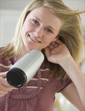 Teenaged girl blow drying hair.