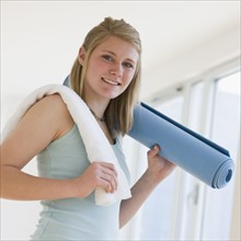 Teenaged girl holding rolled yoga mat.