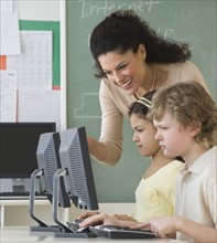 Hispanic teacher helping students with computers.