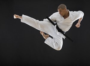 Hispanic male karate black belt kicking in air.
