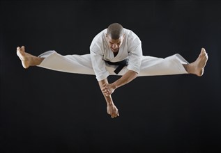 Hispanic male karate black belt jumping in air.