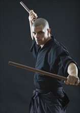 Hispanic male holding sticks in fighting stance.