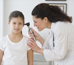 Hispanic female doctor examining child’s ear.