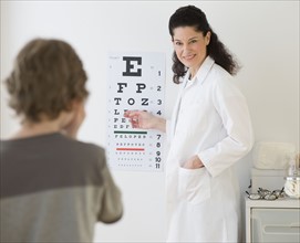 Hispanic female doctor pointing at eye chart for child.