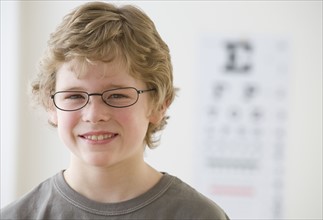 Boy wearing eyeglasses in front of eye chart.
